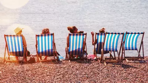 Människor sitter på solstolar på en strand.