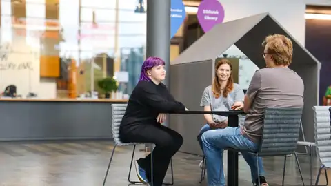 Three people sitting around table discussing.