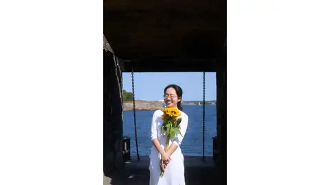 Woman holding sunflowers with the sea in the background.